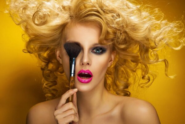 Blond woman applying makeup with brush.